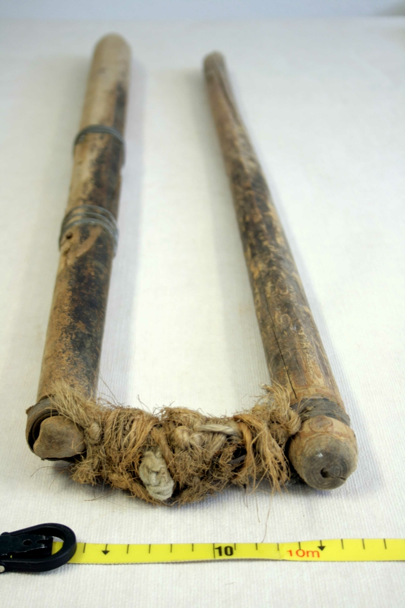 To trestokker som er festet sammen med lærremmer og hampetau, den ene stokken er forsterket med ståltråd.