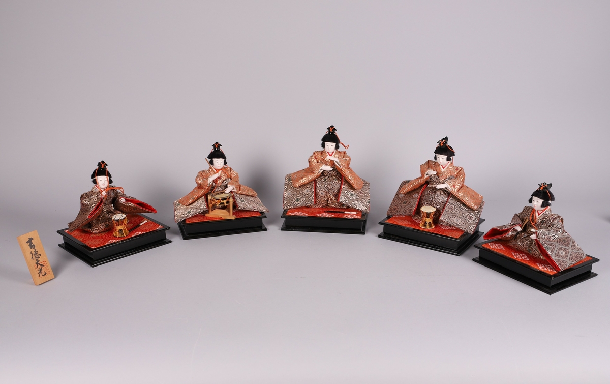 5 dukker med drakter vevet av silke- og gulltråder, sittende på paller av sort lakkert tre på oversiden trukket med stoff.
Dukkene fremstiller musikanter spillende på henholdsvis Kotsuzumi (A), Shime daiko (B), Shinobue (C) og Otsuzumi (D), den femte med en vifte (E).