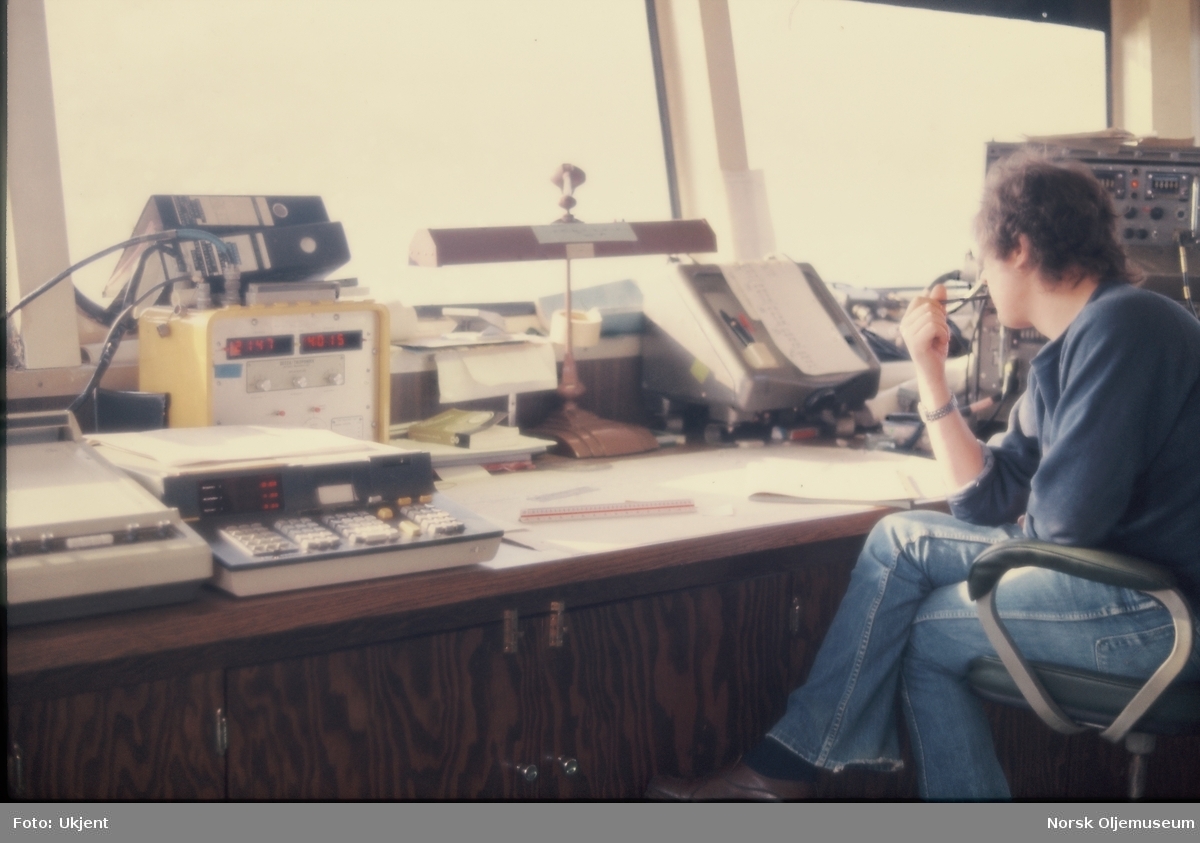 En mann sitter med arbeidstegninger og ulike instrumenter foran seg på ei skipsbro.