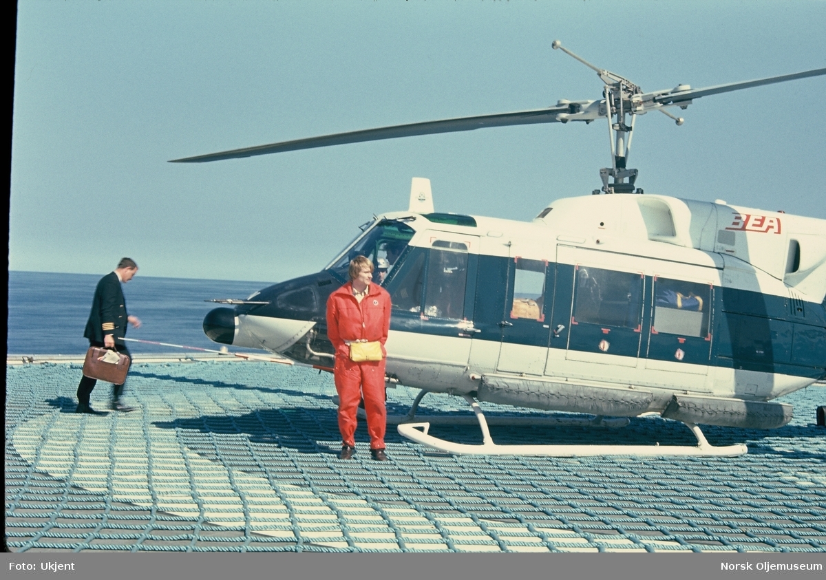 En kaptein og en offshore-arbeider i arbeidstøy utenfor et helikopter på en heliport offshore.