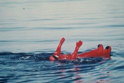 En mann i overlevelsesdrakter ligger i sjøen under en rednin
