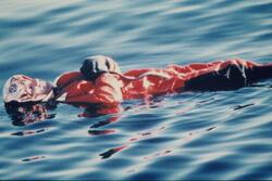 En mann i overlevelsesdrakter ligger i sjøen under en rednin