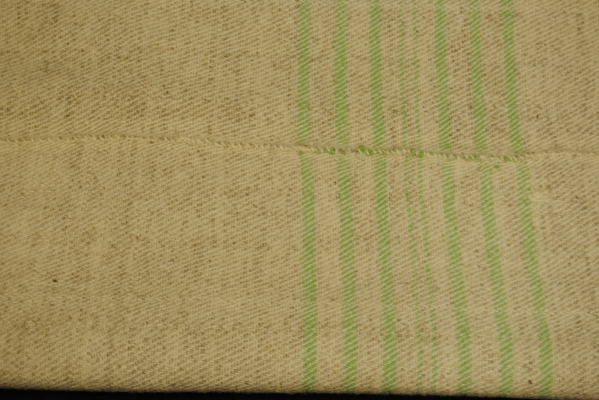 Eit stort kvitel i melert ullstoff med striper i lys grøn. Sydd saman av to delar. Endane er sydd for hand med tjukk lyseblå tråd.