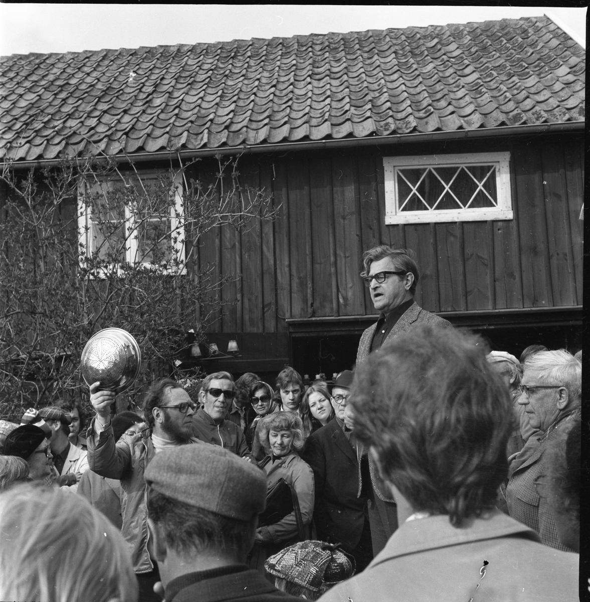 Auktionsutroparen John Karlsson i en folksamling. En man till vänster håller upp möjligen en durkslag i metall.