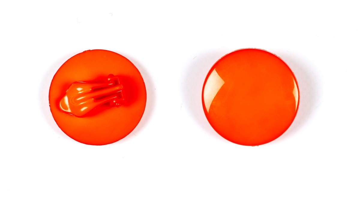 Et par oransje sirkelformede plastøredobber med  klips i samme fargede plast på baksiden.