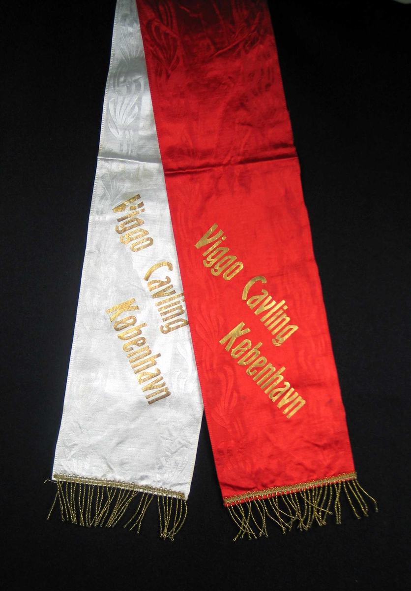 Begravelsessløyfe i hvit og rød silke med tekst og frynser i gull.