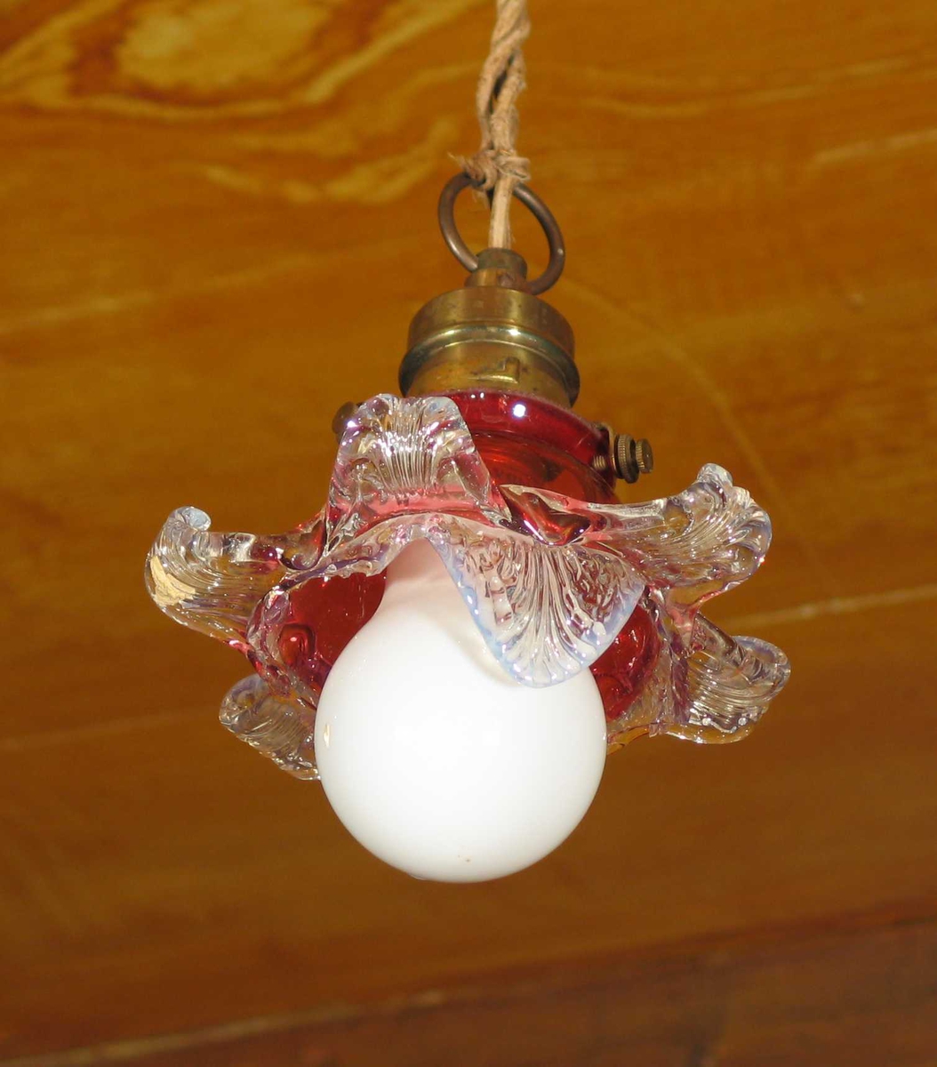 Taklampe i metall med lys rød bladformet glasskjerm. Henger i gammel vridd ledning og er ikke i bruk.