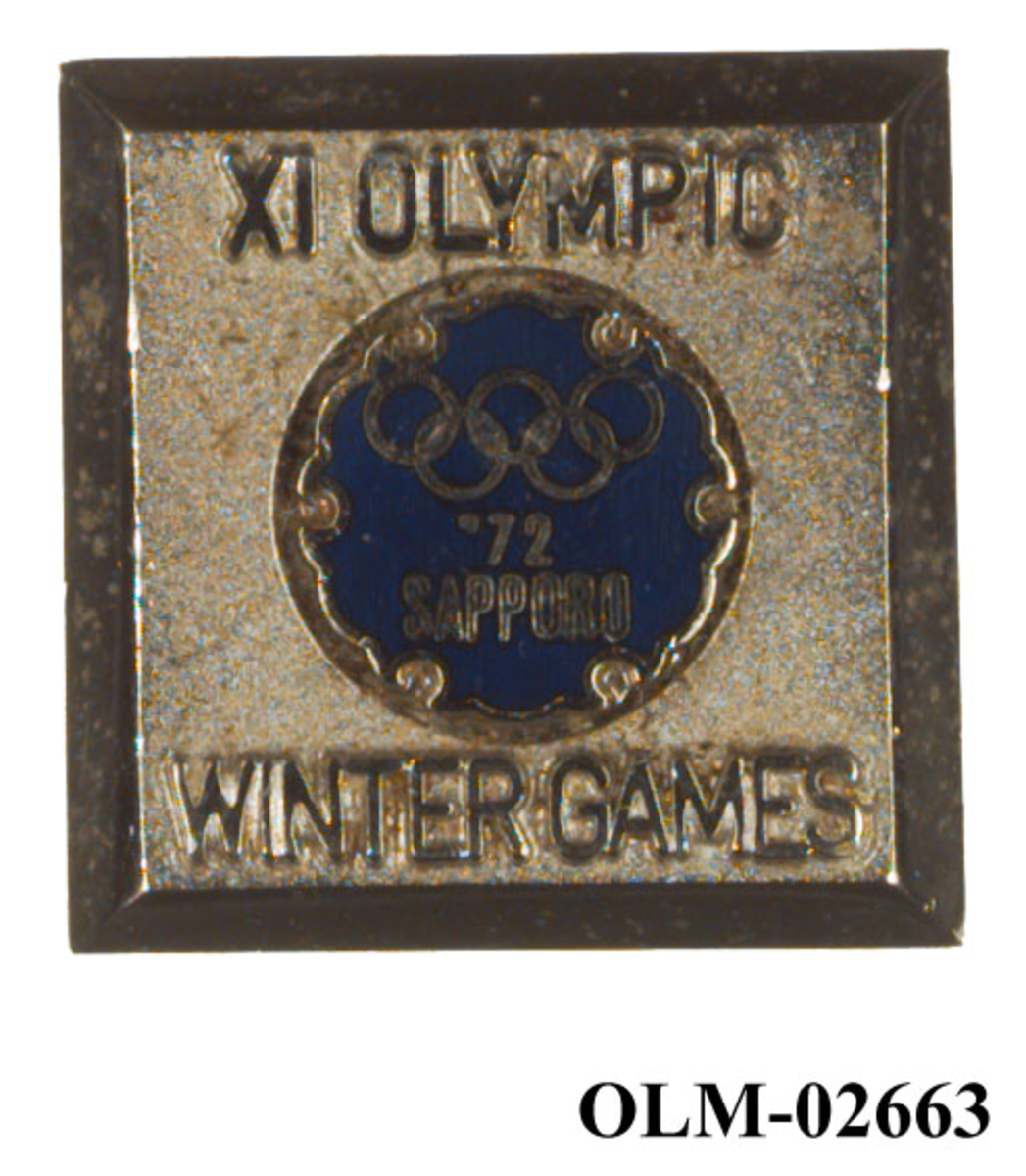 Sølv- og blåfarget pins med motiv av de olympiske ringene.