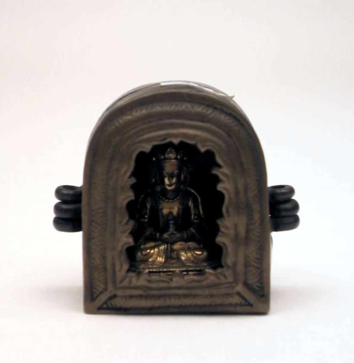 En liten statue av en sittende Buddha plassert i et skrin med åpning. Åpningen mangler glass. Skrinet er av kobber og messing. Buddhafiguren er forgylt.