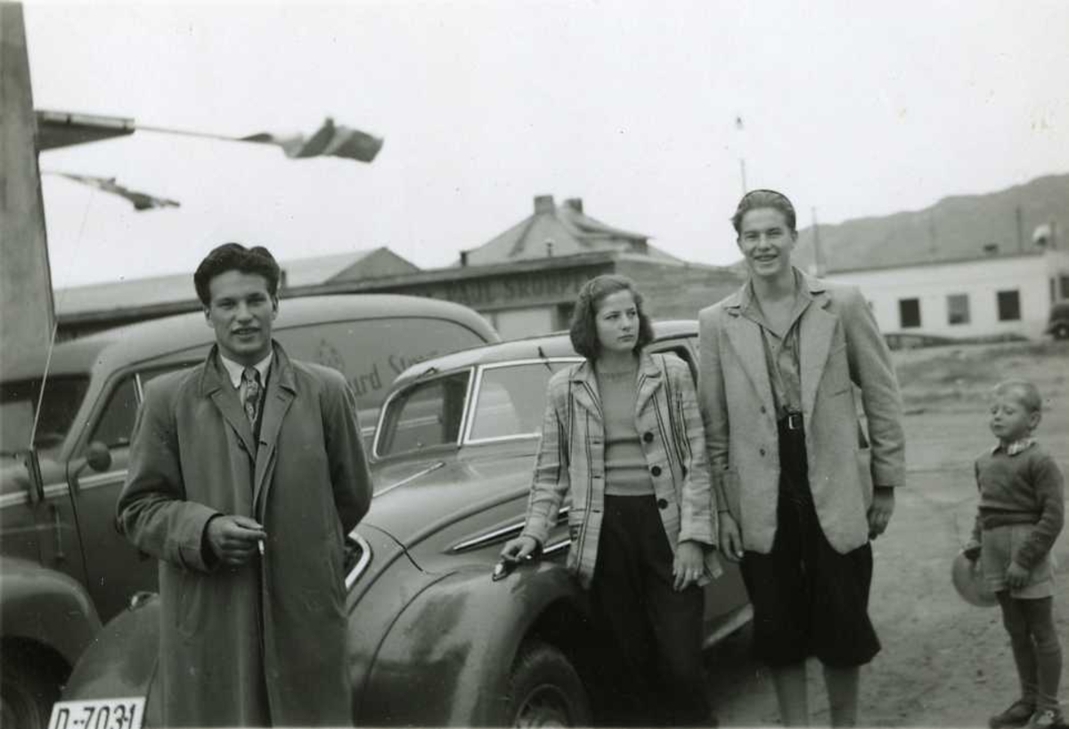 Menn, kvinne, barn, biler. Bilen til høyre en Peugeot 402, årsmodell 1936-39.