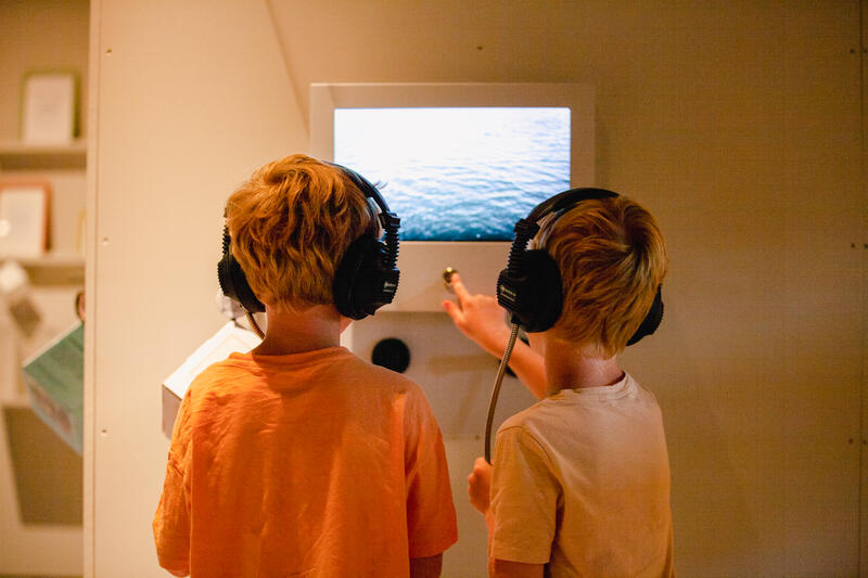 To barn trykker med hodetelefoner trykker på en skjerm i utstillingslokale. (Foto/Photo)