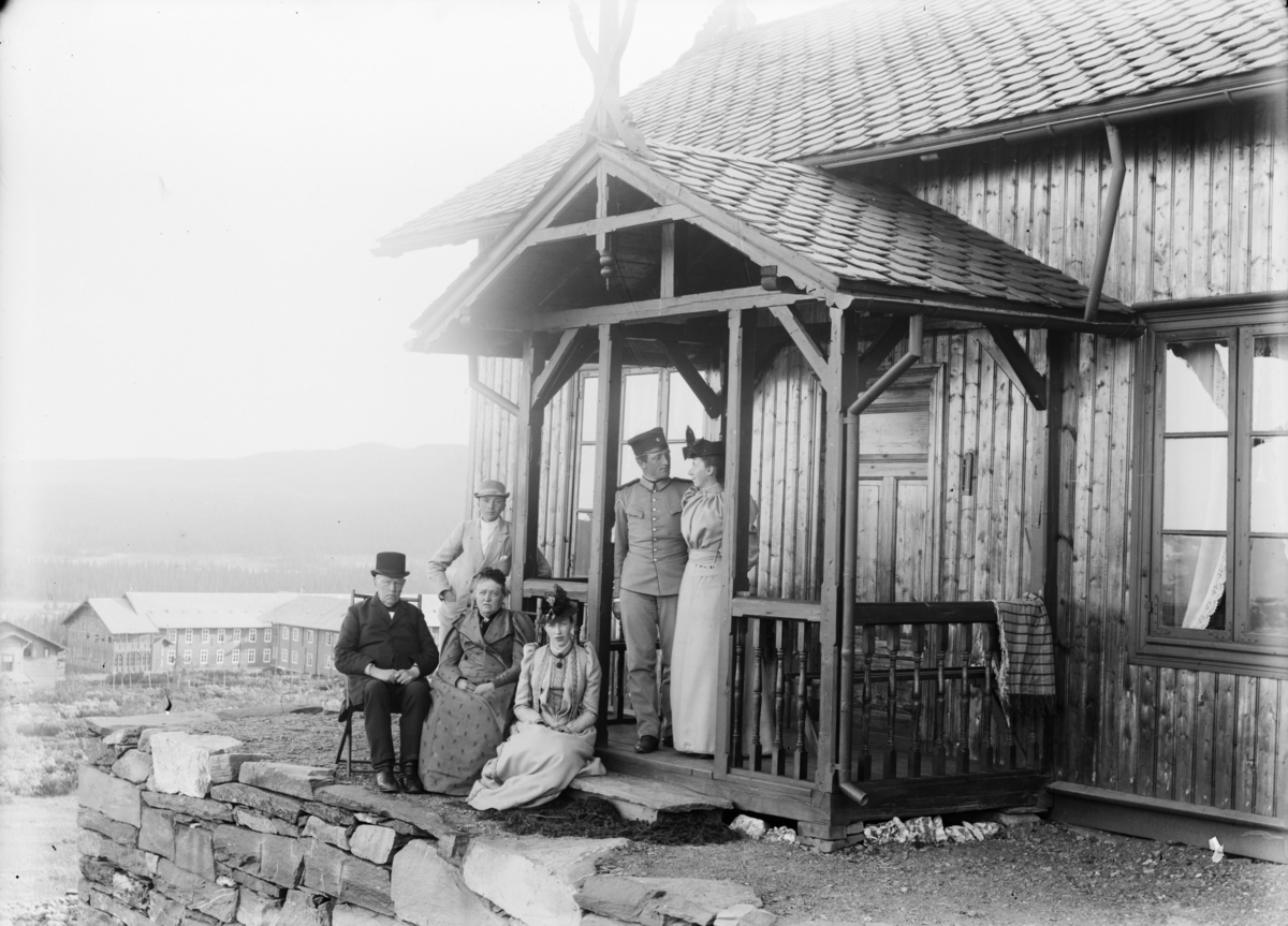 Personer utenfor hytta "Sommerkvil" med gaustad Sanatorium i bakgrunnen. En av mennene i uniform