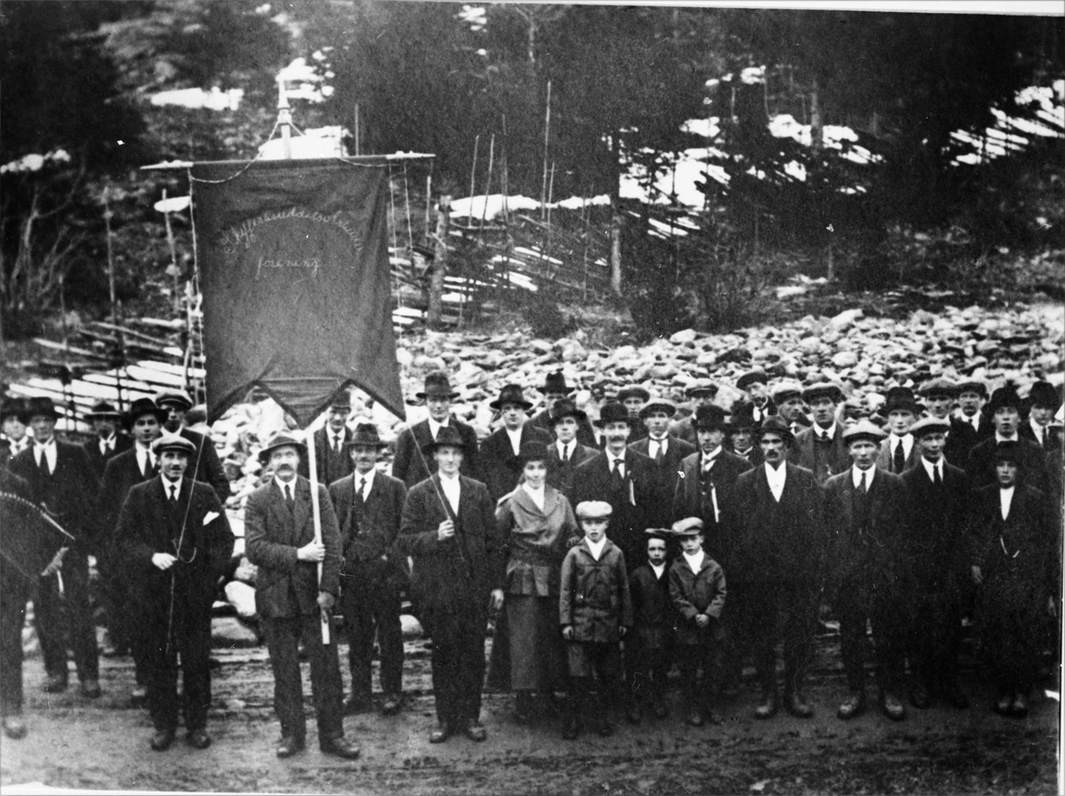Gruppebilde av arbeidsforeningen ved Valdres Skiferbrud. Mannen i forgrunnen holder fanen.