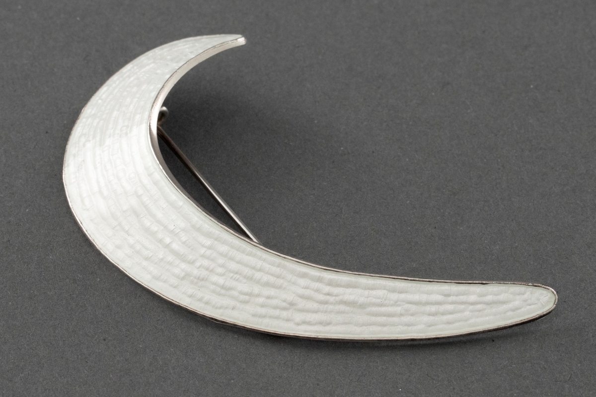En halvmåneformet brosje i sølv sterling med hvit speilemalje.
