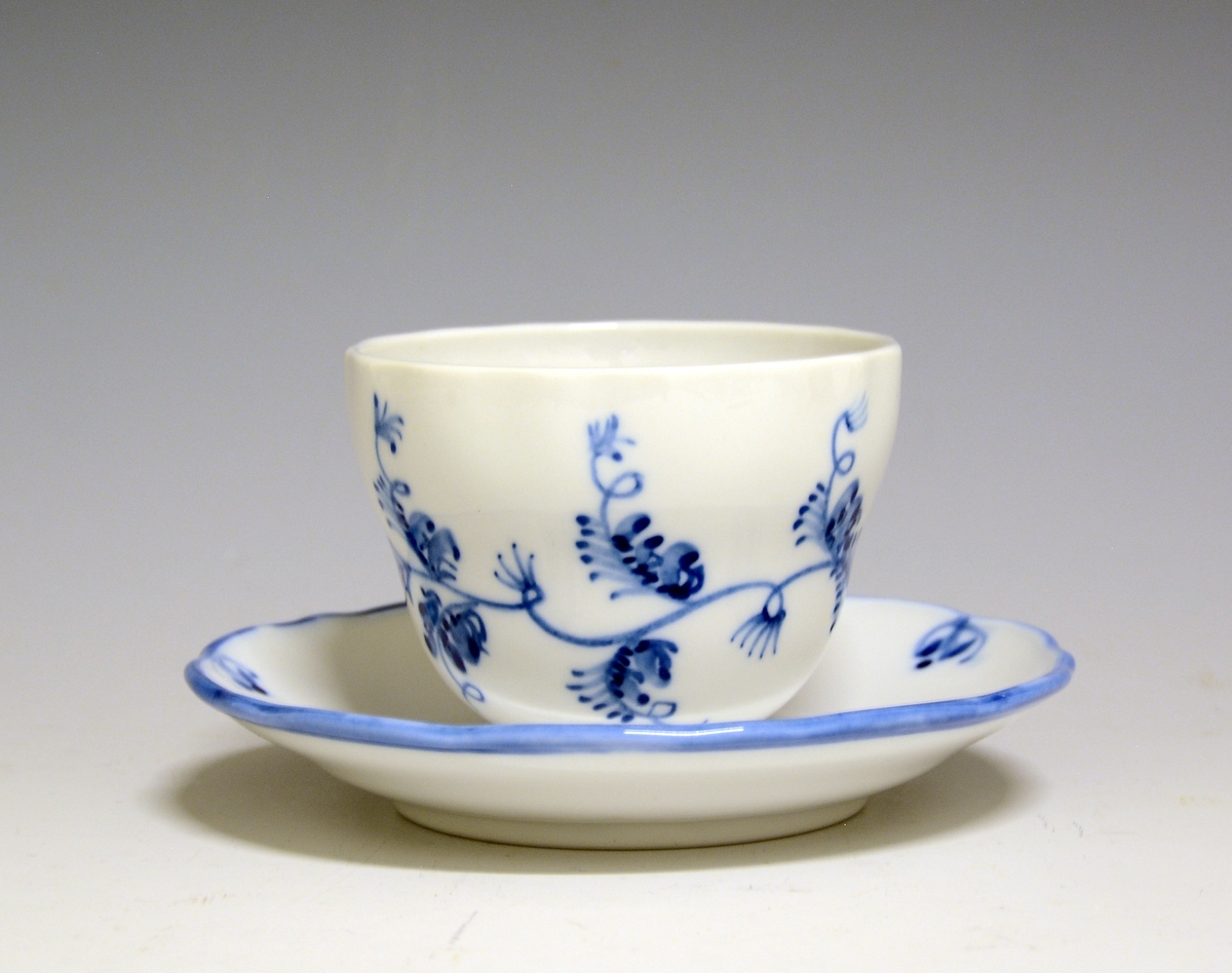 Kaffeskål av porselen. Hvit glasur. Håndmalt blå underglasurdekor på fanen, blå kantstrek ytterst.
Modell: Victoria, 1800
Uten fabrikkmerke.