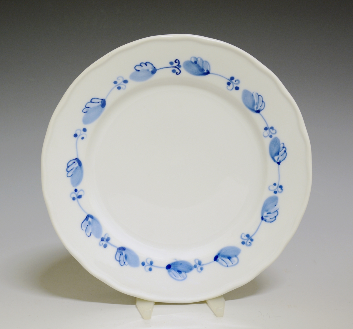 Liten tallerken av porselen. Hvit glasur. Håndmalt underglasurdekor i blått på fanen 
Modell: Victoria, 1800
