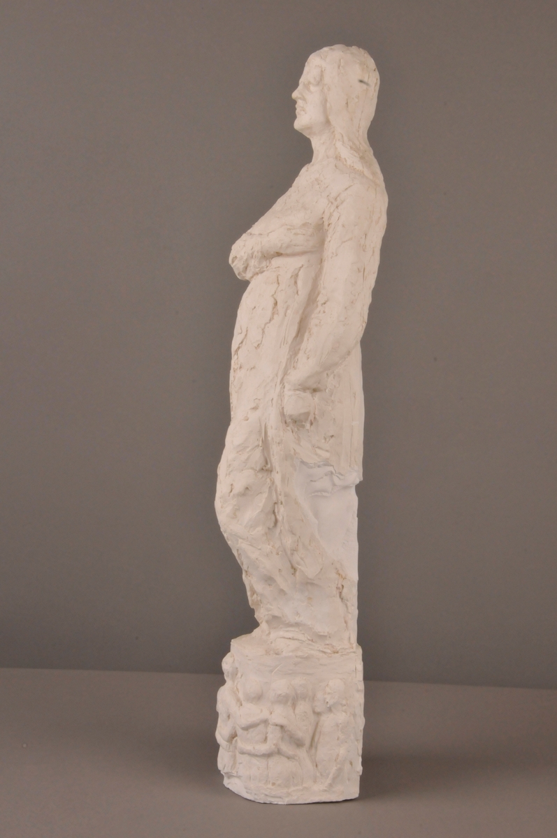 Figur med høgre hand lagt over brystet, venstre heng langs sida. På sokkel: Figurar som held kvarandre i hendane.
