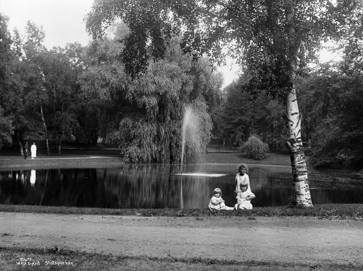 Parti fra Slottsparken, et av tjernene med fontene, tre barn ved vannkanten, i bakgrunnen to kvinner.