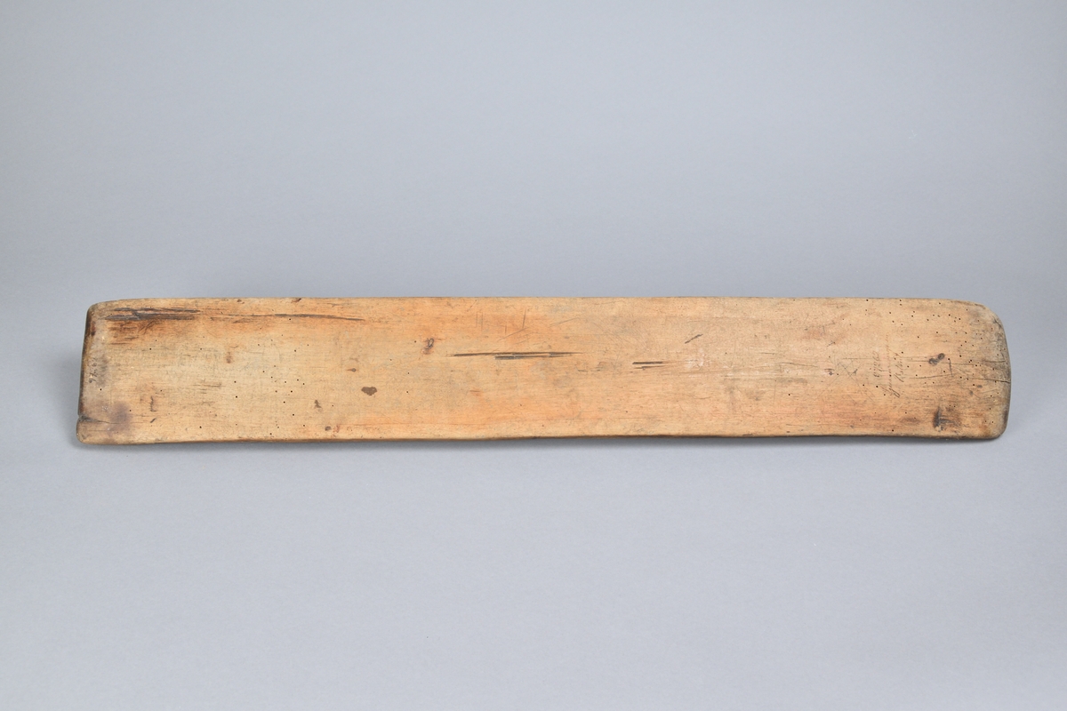 Kavelbräde tillverkat i trä, med rak och rektangulär form. Med handtag skuret från samma stycke. Ovansidan lätt profilerad med ett flertal inristningar, bland annat årtalet "1728". 