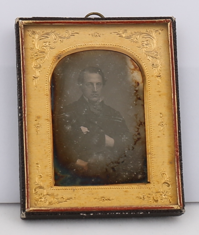 Portrett av mann innrammet bak glass og blomsterornamentert passepartout. Opphengsring på baksiden.