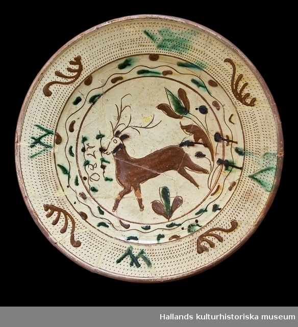 Fat av glaserat lergods i gult, brunt och grönt. Dekorerad med en lekfullt skuttande hjort omgiven av växtslingor och geometriska mönster. Märkt: 1780.