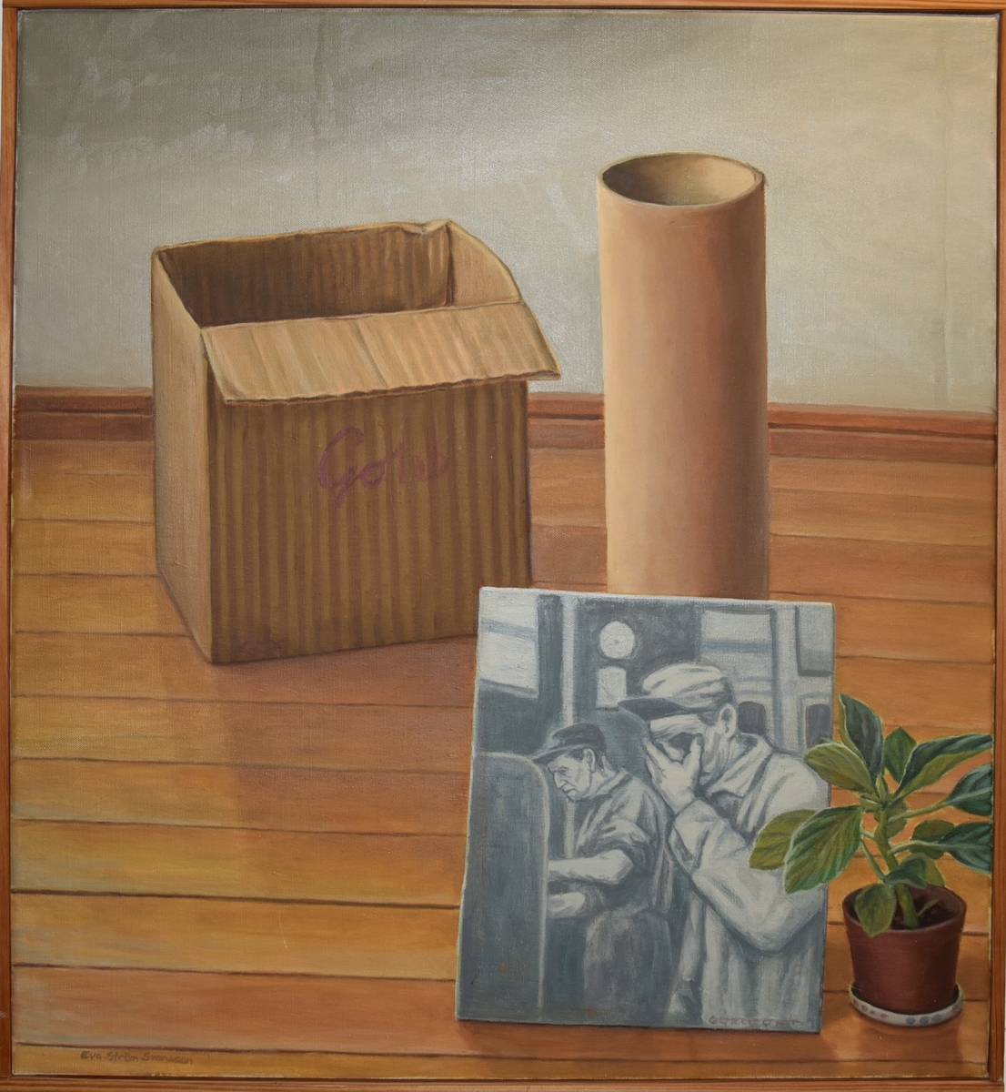 På ett gulbrunt parkettgolv står en papplåda, en papprulle, ett svartvitt foto av två arbetare, samt en krukväxt.