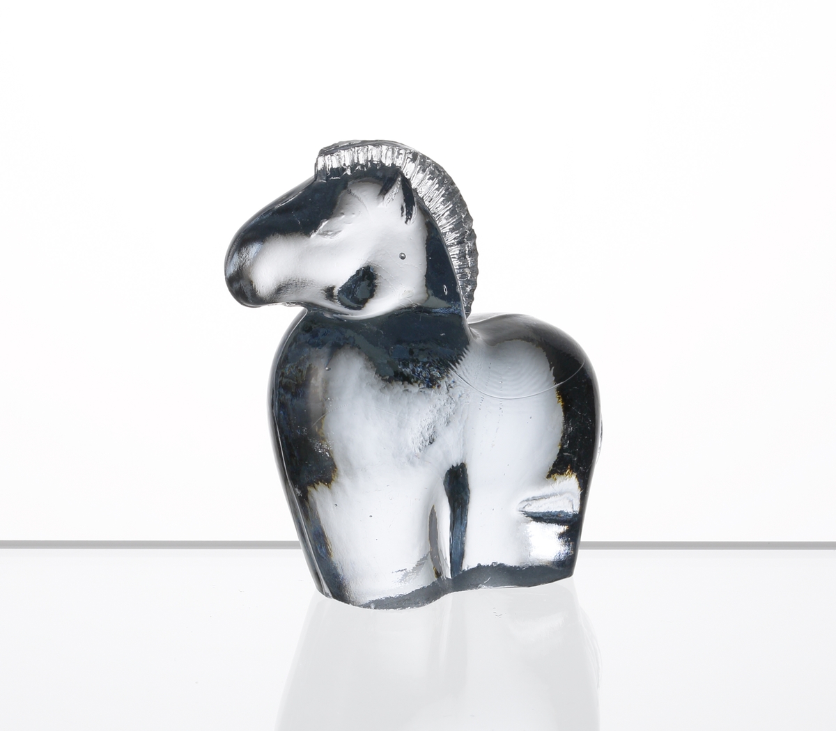 Formgiven av Kjell Blomberg. Mindre figuring i svagt blåtonat glas, föreställande en häst.

