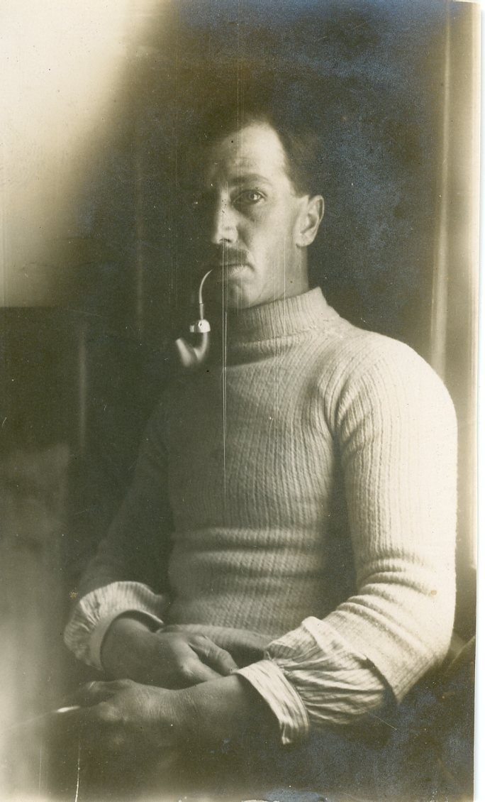 En man med ribbstickad tröja och en pipa i munnen.