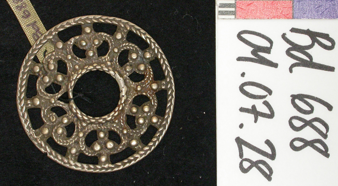 Bd 688 Sølje ("kringlesølje") av sølv. Støpt efterligning av filigran. Rund.