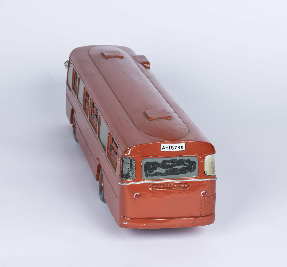 Tremodell av Oslo Sporveiers buss A-15730. Modellen er malt rød, med en hvit stripe langs siden. Bussen har detaljerte utskjæringer for dører og vinduer, og detaljer på taket. 