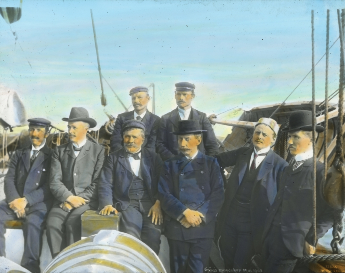 Håndkolorert dias. Gruppeportrett av mannskapet på Gjøa. Sommeren 1903 seilte Roald Amundsen ut fra Oslo med skuta Gjøa. Målet for ekspedisjonen var Nordvest-passasjen.