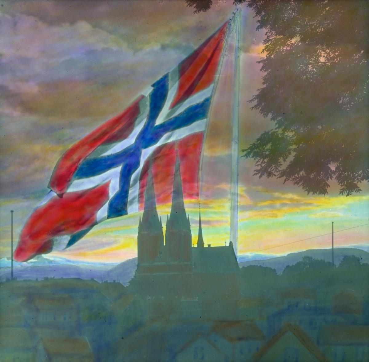 Håndkolorert dias. Utsyn over Skien og Skien kirke. Et stort norskt flagg, heist på en flaggstang, er malt over det mørke bylandskapet og dekker store deler av himmelen, som er farget av solnedgang. Til høyre i forgrunnen ses grenene på et tre.