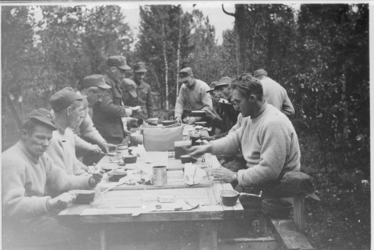 Soldater på Setermoen har matpause ved et bord utendørs.