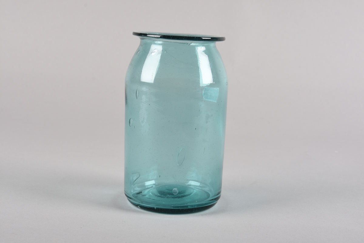 Sylindrisk støypt glaskrukke. Korpus svingar inn mot toppen og deretter ut til ein krage ved munningsranda. Glaset er produsert av resirkulert glas og har fleire luftboblar i godset. Lett grønfarga.