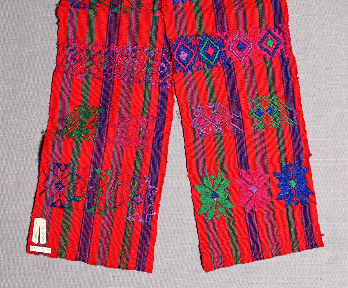 Brett vävt bälte från Santa Maria de Jesus, Guatemala. Hör till kvinnodräkten. 
Rödrandig panama med inplockade mönster i grönt, blått, och två lila nyanser.