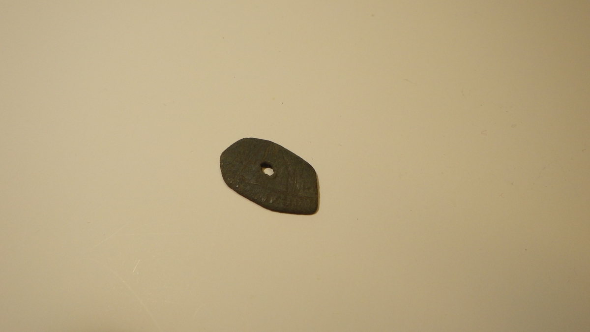 Avlang liten plate med klipte kanter og et naglehull i midten. Gjenstanden kan er ut til å ha strekdekor.