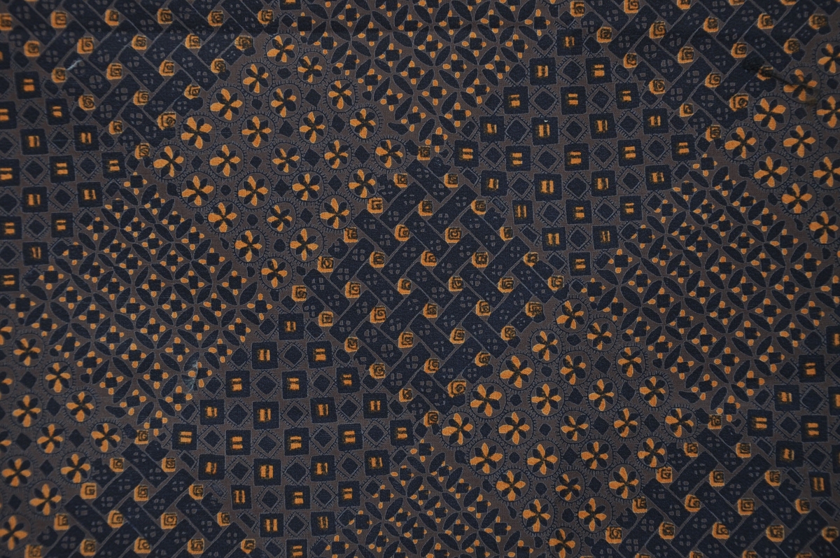 Bomullstyg, början av 1960-talet.
Klänningstyg på 90 cm bredd. Tryckt småmönstrat mönster med patchwork-effekt i bruna toner och inslag av orange.
Otvinnat garn.
Rapport 21,3 x 20,5 cm.
Tryckfärger 2.