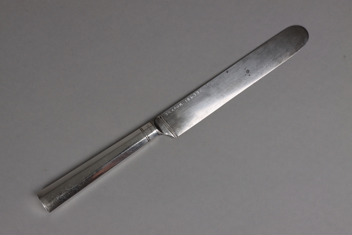 Bordskniv av stål med facetterat skaft av silver. Vid fäste för knivblad dubbla linjer runt om. Skaft med rakt avslut.

