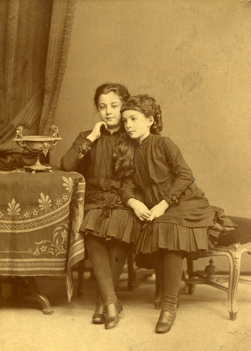 To jenter sittende i et fotostudio. Trolig Sandra Droucker og et søsken.