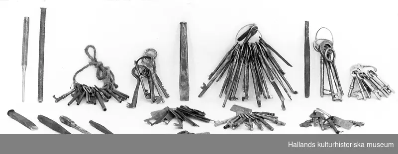 Verktygslåda med nycklar och verktyg. Se även invnr 031401a-ö. 
a) Nyckelknippa. Ståltrådsring med tio nycklar av olika storlekar. Längsta nyckelns längd 8 cm. Kortaste nyckelns längd 4,1 cm. 
b) Nyckelknippa. Ståltrådsring med sju nycklar i olika storlekar. Längsta nyckelns längd 6,5 cm. Kortaste nyckelns längd 3 cm. 
c) Nyckelknippa. Ståltrådsring med sex nycklar i olika storlekar, varav fem är handsmidda. Längsta nyckelns längd 10,7 cm. Kortasta nyckelns längd 7,2 cm. 
d) Nyckelknippa. Ståltrådsring med nio nycklar. Nyckel längd 6,6 cm. 
e) Nyckelknippa. Ståltrådsring med sexton platta, handgjorda nycklar i olika storlekar. Längsta nyckelns längd 8,5 cm. Kortaste nyckelns längd 4,2 cm. 
f) Nyckelknippa. Ståltrådsring med fyra nycklar i olika storlekar, varav tre är handsmidda.  Längsta nyckelns längd 12,2 cm. Kortasta nyckelns längd 9,2 cm. 
g) Nyckelknippa. Ståltrådsring med tjugosex handsmidda nycklar i olika storlekar. Längsta nyckelns längd 13 cm. Kortasta nyckelns längd 7,6 cm. 
h) Nyckelknippa. Ståltrådsring med åtta nycklar i olika storlekar. Längsta nyckelns längd 5,2 cm. Kortasta nyckelns längd 4,7 cm. 
i) Nyckelknippa. Snöre med femton nycklar i olika storlekar. Längsta nyckelns längd 9,5 cm. Kortasta nyckelns längd 2,9 cm. 
j) Huggmejsel, handsmidd, järn. Längd 14,6 cm. Diameter 1,5 cm. 
k) Huggmejsel, handsmidd, järn. Längd 9,6 cm. Diameter 1,5 cm. 
l) Körnare, handsmidd, järn. Längd 14,4 cm. Diameter 1,3 cm. 
m) Järnrör. Tillplattat i ena änden. Längd 17,4 cm. Diameter 1 cm. 
n) Verktyg, handsmitt, av järn. Längd 14,2 cm. Bredd 1,9 cm.  (Teckning) 
o) Verktyg, handsmitt, av järn. Längd 11,2 cm. Bredd 1 cm. (Teckning) 
p) Verktyg av järn Längd 14,2 cm. Bredd 1,9 cm. Fabriksmärke?  (Teckning)  
q) Verktyg, handsmitt av järn. Längd 9,5 cm. Diameter 1 cm.  (Teckning)