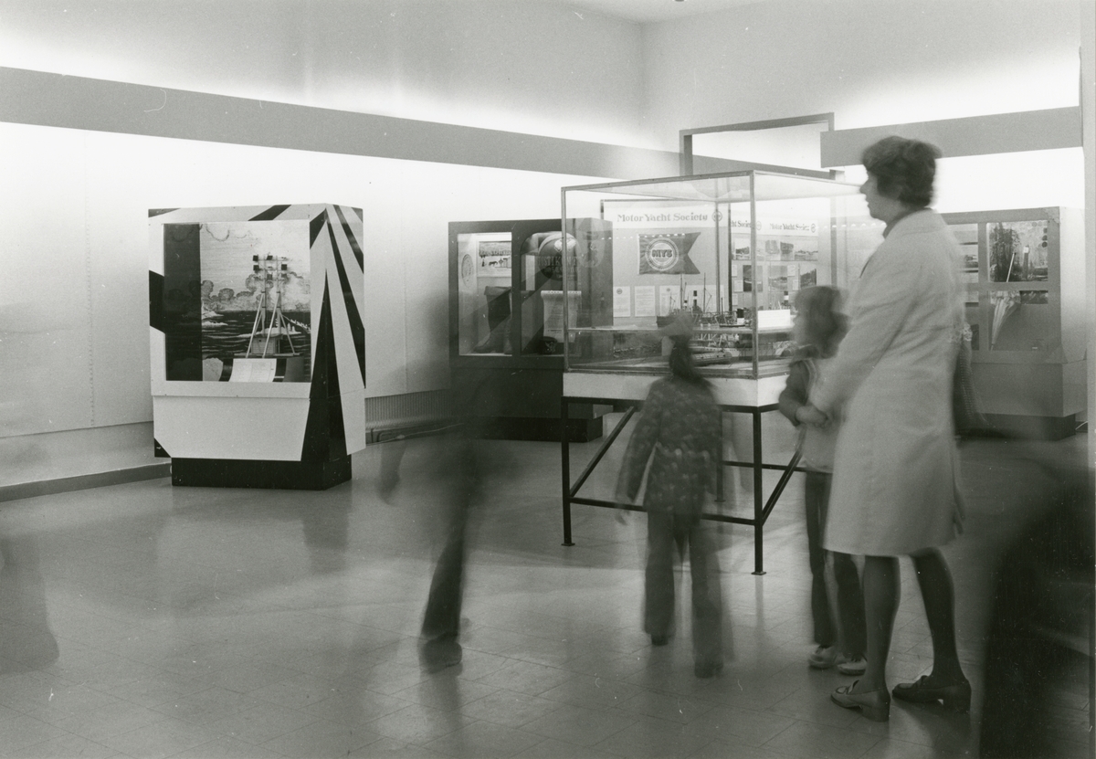 Utställningen "Post över Ålands hav". En kvinna besöker utställningen. På bilden synns även fyra barn i rörelseokärpa.