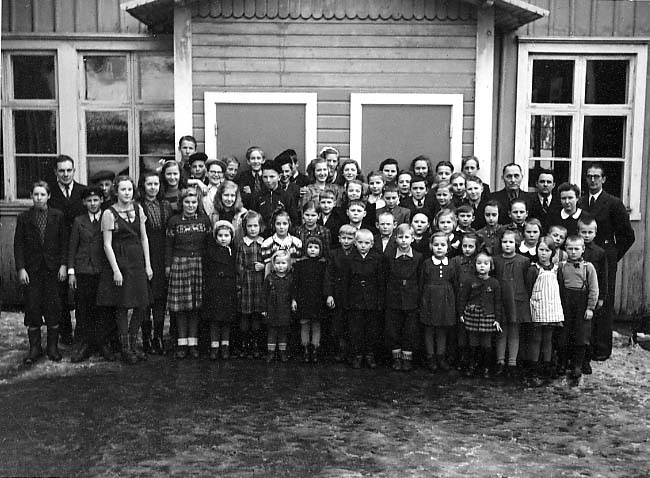 En estnisk skolklass med flickor och pojkar i olika åldrar samt manliga lärare på gårdsplanen till Folkskolan i Gränna.