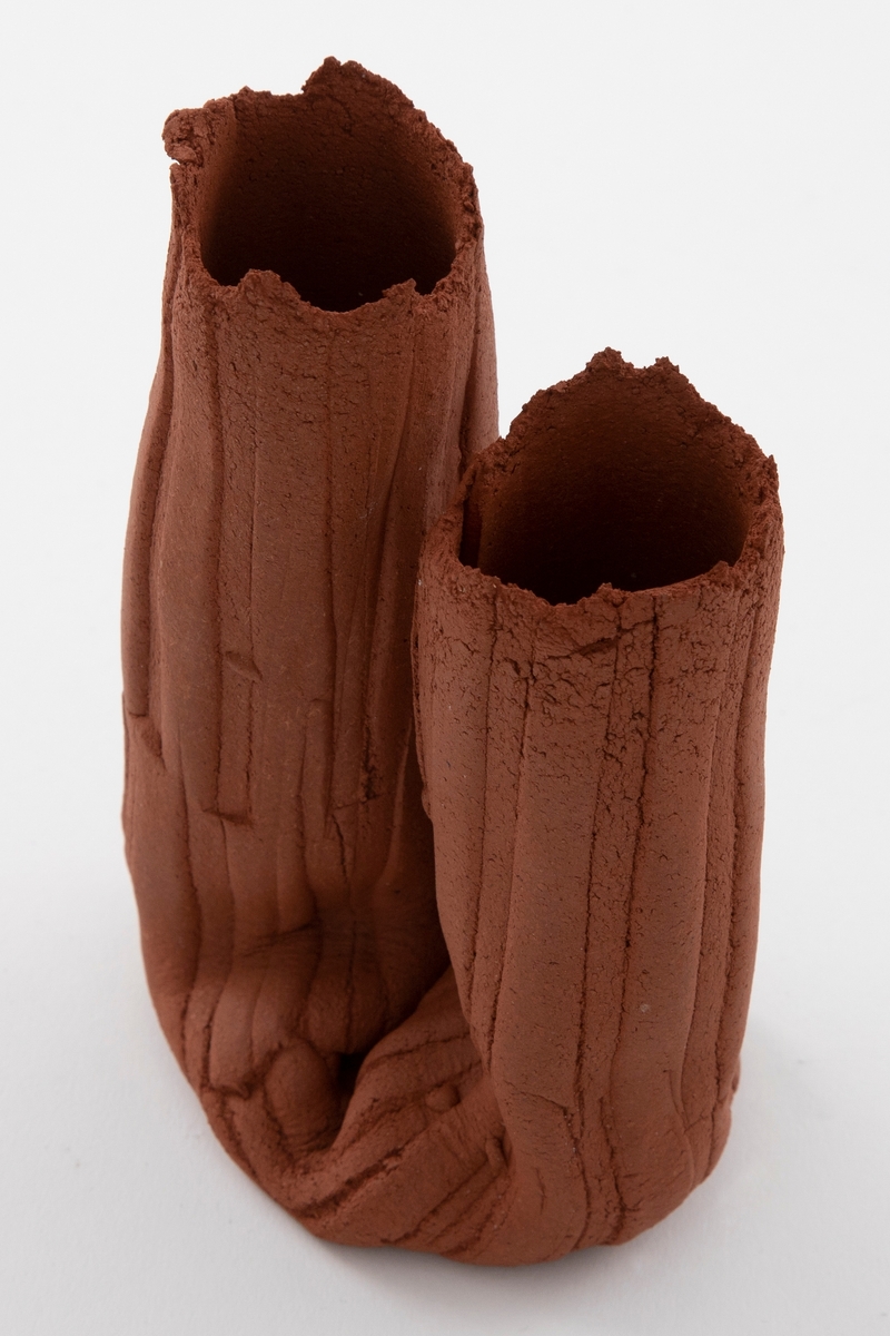 Matt rødbrun vase i steingods. Sammenklemt, asymmetrisk U-form med vertikale, brede riller. Åpne munninger med ujevne render.