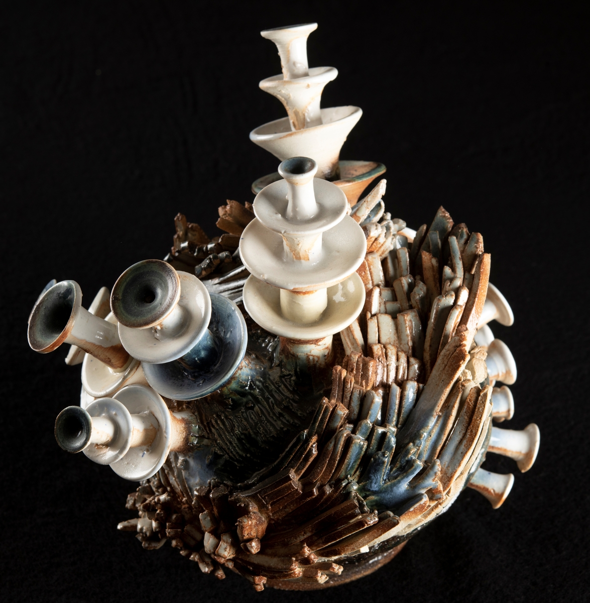 Stengodsobjekt bestående av ett antal trumpetliknande stjälkar som reser sig ur ett fundament bestående av strimlor av keramik lagda i en klump.