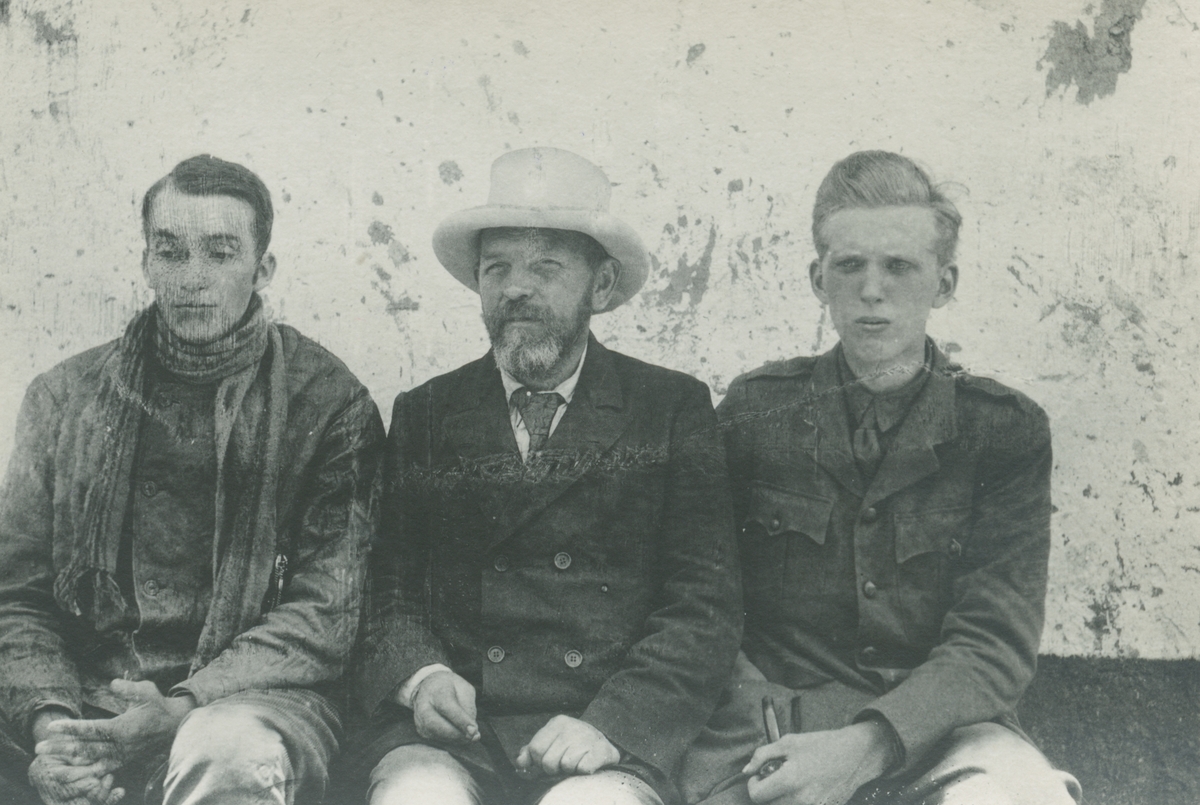 Fotografi från expedition till Peru 1920. Porträtt av tre män som sitter framför husvägg. Mannen i mitten är Otto Nordenskjöld.
