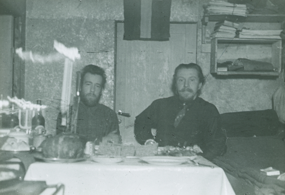 Glasnegativ med motiv av två män som äter en måltid vid ett matbord.