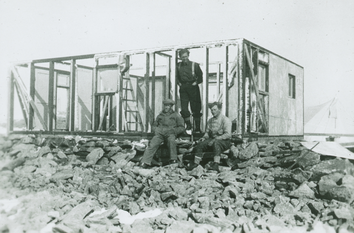 Glasnegativ med motiv av tre män framför husbygge.