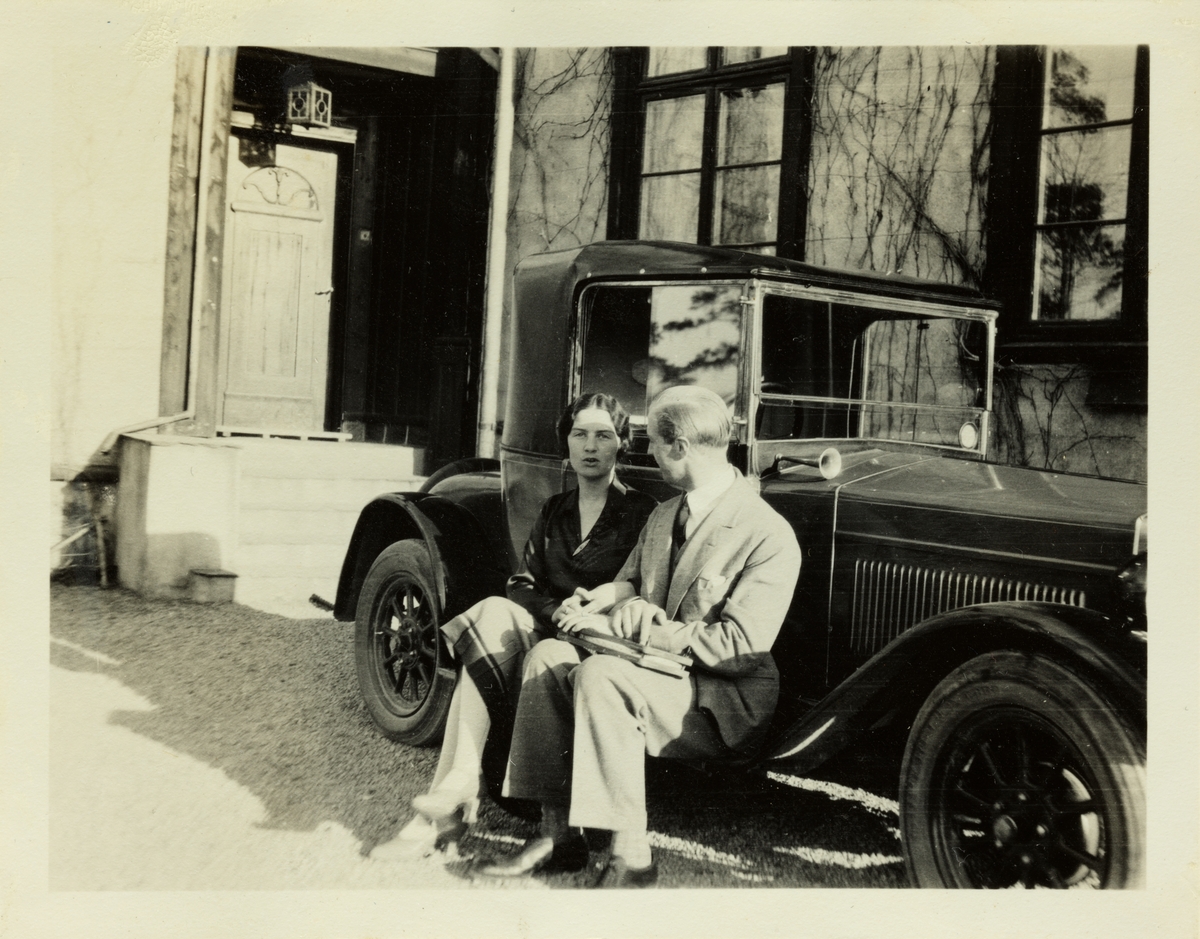 Et ungt par, antagelig Lucy Egeberg og forloveden Anton Fredrik Klaveness, sitter på stigbrettet til en bil på eiendommen Lagåsen i Bærum. fotografert juni 1928.