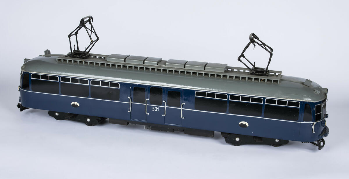 Tremodell i en mørk blå farge, med sorte vinduer og grått tak av forstadsbane fra Bærumsbanen med nr. 301. Modellen har detaljerte utskjæringer og malingsdetaljer som gjør den tro til originalen. På taket er to pantografer til kontaktledningen. 