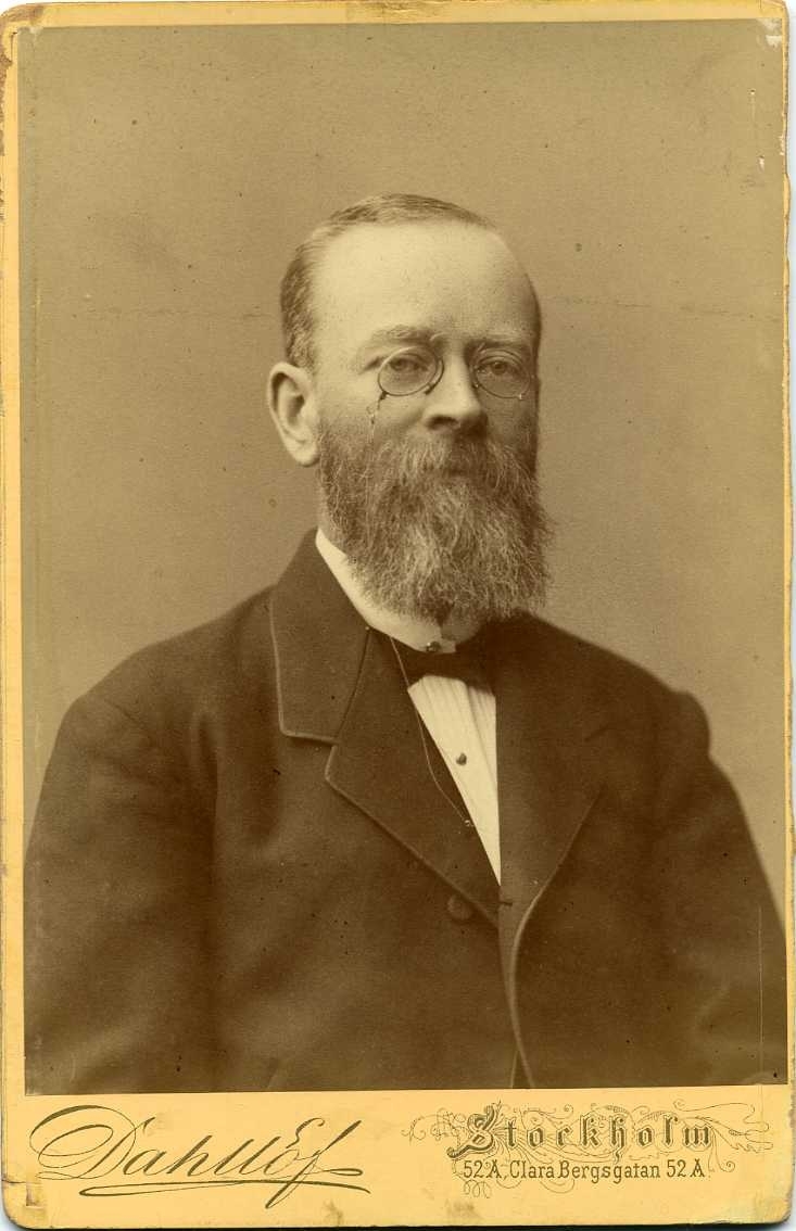 Porträtt av en man med glasögon och skägg.